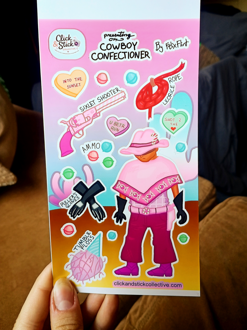 First person view of a hand holding the Cowboy Confectioner sticker sheet.